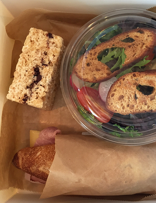 overhead view of the boxed lunch with treat, salad, and wrapped sandwich